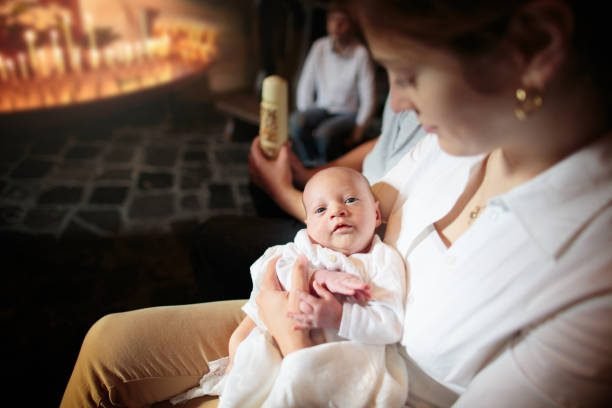 Mother holding a baby beside a baptismal candle